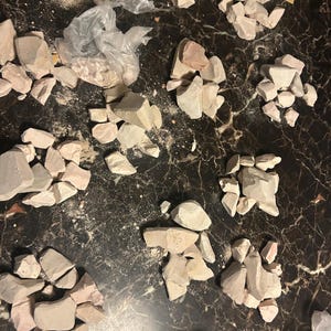 May include: Multiple piles of light pink and white clay rocks on a dark brown surface.