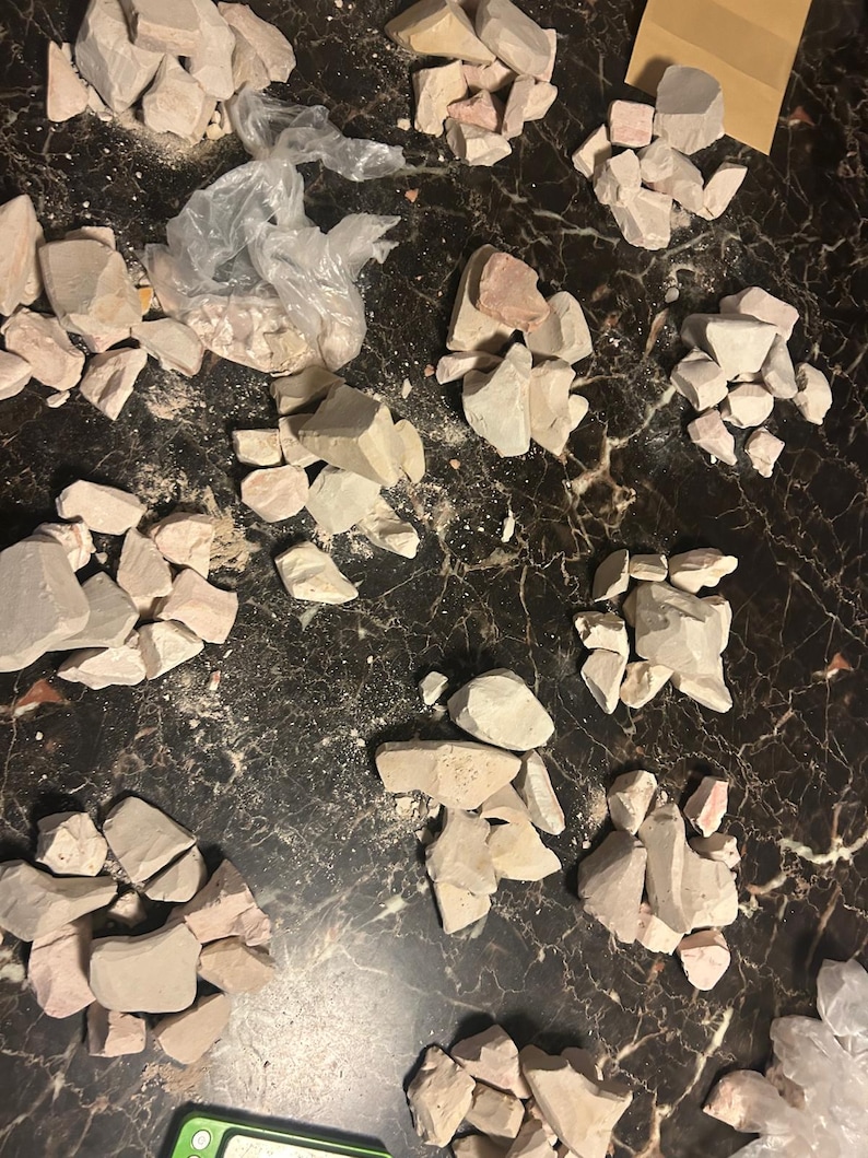 May include: Multiple piles of light pink and white clay rocks on a dark brown surface.