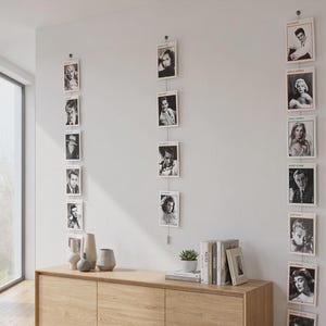 Könnte beinhalten: Ein Sideboard aus hellem Eichenholz mit drei Schranktüren, auf dem eine kleine Sukkulente im Topf und mehrere Bücher stehen. Drei vertikale Hängedrähte sind an der Wand befestigt, an denen jeweils eine Reihe schwarz-weißer Porträtfotos hängt.