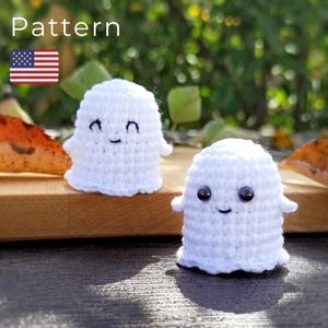 May include: Two handmade white crochet ghost figures with smiling faces and small arms. One ghost has black embroidered eyes and a curved mouth. The other ghost has black button eyes and a curved mouth. The word "Pattern" is in the top left corner.