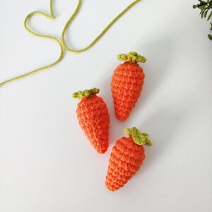 May include: Three crocheted carrots with green tops. The carrots are orange and the tops are green. The carrots are arranged in a triangular shape on a white background.