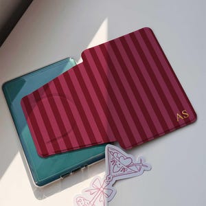 May include: A red and pink striped phone card holder with gold initials and a pink martini sticker. The phone case is teal and clear. The sticker has a martini glass design with hearts and bows.