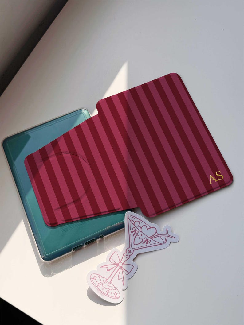 May include: A red and pink striped phone card holder with gold initials and a pink martini sticker. The phone case is teal and clear. The sticker has a martini glass design with hearts and bows.