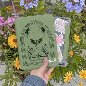 May include: A sage green tablet case featuring a dragon design within an arched window frame, with the text "Fourth Wing of the Broken" and "cheal". A second case with book stickers is visible.