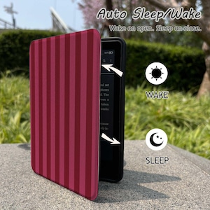 May include: A burgundy and dark red striped e-reader cover with the text "Auto Sleep/Wake" and "Wake on open. Sleep on close." The cover is open, revealing the e-reader screen. The image also shows a sun icon labeled "WAKE" and a moon icon labeled "SLEEP".
