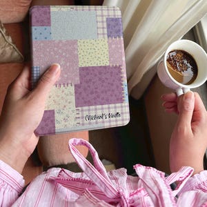 May include: A Kindle cover with a patchwork design in shades of purple, pink, and blue. The cover features various floral and plaid patterns. The text "Micheal's kindle" is printed on the cover.