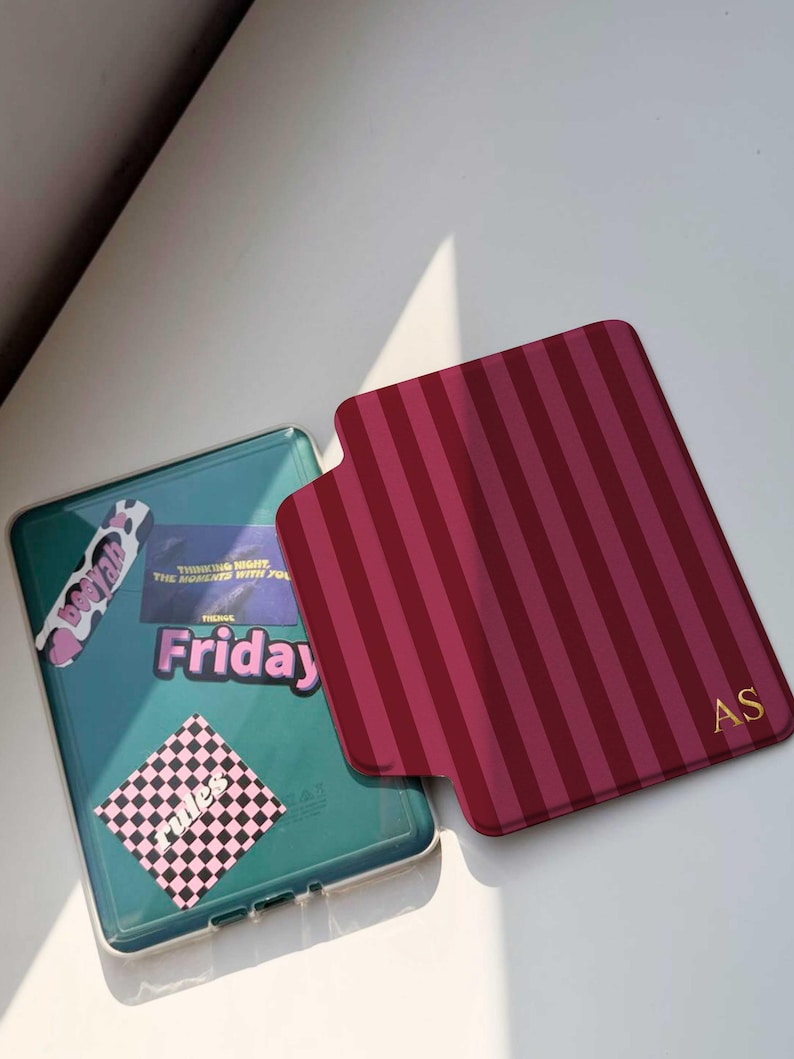 May include: Two phone cases. One is teal with stickers that say "Friday", "Thinking Night The Moments With You", and "Be You". The other is burgundy with vertical stripes and gold initials "AS".