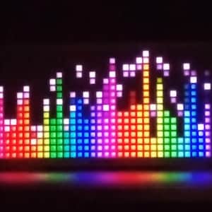 Può includere: Un display LED rettangolare che mostra un grafico di equalizzazione colorato. Il display presenta uno spettro di colori, tra cui rosso, arancione, giallo, verde, blu e viola, disposti in un motivo a grafico a barre verticali. Le luci sono luminose.