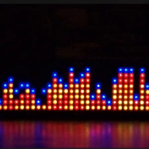 Op de afbeelding: Een digitale audiospectrumvisualisator met een raster van verlichte ledlampjes. Het display toont verticale balken van variërende hoogtes in de kleuren rood, oranje, geel en blauw tegen een effen zwarte achtergrond.