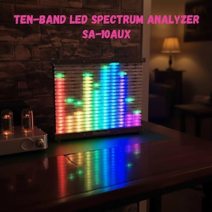 Puede incluir: Un analizador de espectro LED de diez bandas, modelo SA-10AUX, muestra un espectáculo de luces multicolor. El dispositivo presenta barras verticales que se iluminan en respuesta a las frecuencias de sonido. Se encuentra sobre una superficie de madera oscura.