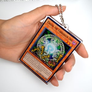 May include: A clear plastic keychain featuring a Yu-Gi-Oh! card with the image of Exodia the Forbidden One. The card is surrounded by a silver chain.