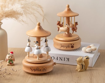 May include: Two wooden music boxes with a carousel theme. One features ballerina figurines, the other has horse figurines. Both are light brown with a domed top and a circular base. The ballerina music box has the name "Sophia" engraved on it.
