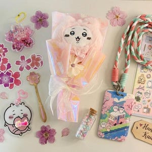 May include: A collection of stationery and accessories including a plush bouquet, a braided lanyard with a character card holder, sticker sheets, acrylic keychains, a gold spoon, a glass bottle with beads, and a tag labelled Handpicked Kawaii.