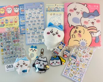 以下が含まれることがあります： ステッカー、ぬいぐるみ、キーホルダー、ピンクのフォルダーなど、カワイイをテーマにしたグッズのコレクション。青と白のアクセントが特徴の漫画のキャラクターが描かれています。ステッカーは様々なサイズと形があります。