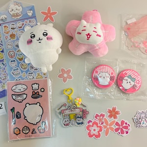 May include: A collection of character-themed merchandise including two sticker sheets, a white plush toy, a pink star-shaped plush, a clear acrylic keychain, two circular pin-back buttons, and several individual die-cut stickers featuring floral motifs.