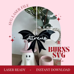 Op de afbeelding: Zwarte vleermuisvormige ornament met de naam "Atreus" in witte letters. Het ornament hangt voor een witte vaas met groen. De afbeelding heeft een roze achtergrond met de tekst "SVG Laser File" en "Burns SVG Studio".