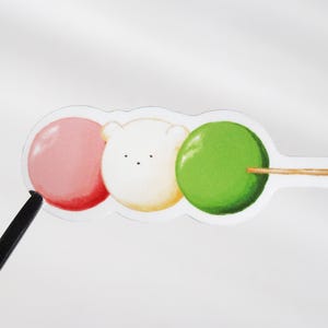 May include: A sticker featuring three round dango-style shapes on a skewer. The left shape is pink, the centre shape is a white bear face with small black eyes and a nose, and the right shape is green. The sticker has a clear border.