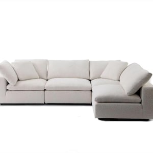 May include: An off-white modular corner sofa with a contemporary design. The sofa is composed of several sections and features soft, square cushions. The fabric has a textured, bouclé finish. It includes several matching scatter cushions, creating a comfortable seating arrangement.