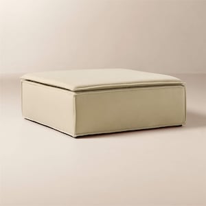 May include: A square, cream-colored ottoman with a padded top and a boxy base. The ottoman is upholstered in a smooth, neutral fabric, and the design is simple and modern. The dimensions are approximately 36 inches long, 36 inches wide, and 18 inches high.