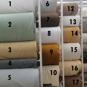 May include: A display of fabric rolls in various colors, including white, green, tan, gray, and gold. The text "Boucle MD Tower" is at the top. The rolls are numbered 1 through 17.