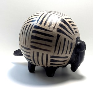 May include: A ceramic sheep figurine with a cream-colored body and black geometric pattern. The sheep has black legs, a black head, and a small tail. The figurine is on a white surface.