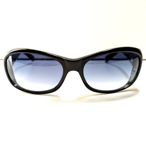 May include: Black sunglasses with a curved frame and gradient blue lenses. The sunglasses have a sleek, modern design, suitable for outdoor activities. The lenses transition from a darker shade at the top to a lighter shade at the bottom.