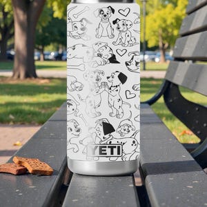 May include: A white YETI tumbler featuring a black and white Dalmatian dog pattern. The design includes various poses of the dogs, bones, and hearts. The tumbler is sitting on a black bench with two brown biscuits.
