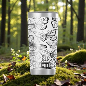May include: A white stainless steel tumbler featuring a repeating black line art pattern of various butterflies. The cylindrical container has a metallic silver rim and base, with the YETI brand logo printed in black at the bottom center.