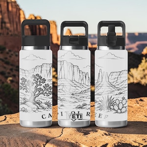 May include: Three white stainless steel water bottles with black lids, each featuring a black line art illustration of a desert landscape. The text CAPITOL REEF and a YETI logo are printed on the bottles, which show rocky cliffs, a tree, and cacti.