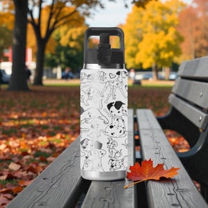 May include: A white water bottle with a black handle and lid, covered in a black and white Dalmatian dog pattern. The bottle is stainless steel and sits on a wooden bench in a park setting.