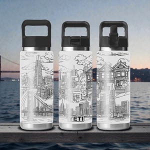 Puede incluir: Tres botellas de agua de acero inoxidable con asas y tapas negras. Cada botella presenta un dibujo lineal en blanco y negro del horizonte de San Francisco, incluyendo el Golden Gate Bridge y la Transamerica Pyramid. La marca "YETI" es visible en una botella.