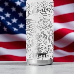 Puede incluir: Un vaso t&eacute;rmico blanco con base plateada, con ilustraciones en blanco y negro de iconos estadounidenses como panqueques y un jugador de f&uacute;tbol americano. Tambi&eacute;n es visible la palabra "HOLLYWOOD".