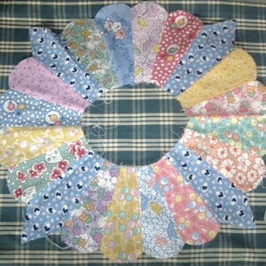 May include: A colorful, handmade fabric wreath with a scalloped design. The wreath is composed of various patterned fabric pieces in shades of blue, pink, yellow, and green. The fabrics feature floral and fruit motifs, creating a cheerful, vintage aesthetic.