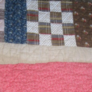 May include: Close-up of a patchwork quilt with various fabric patterns. The quilt features sections of blue floral, plaid, and dotted patterns, along with a pink floral and beige striped fabric. The quilt is quilted with a diamond pattern.