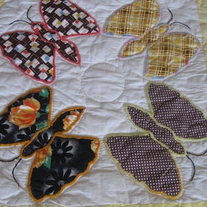 May include: A handmade quilt featuring six butterfly appliqués in various patterns and colors. The butterflies are arranged around a central white circle on a white background, with a yellow border.