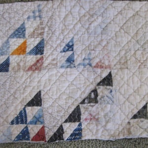 May include: Cream-colored quilt with a repeating pattern of triangles in various colors, including blue, red, and orange. The quilt has a diamond-stitched pattern throughout. The triangles are arranged in a stepped pattern.