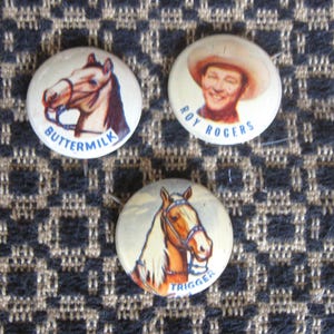 May include: Three vintage pinback buttons featuring Western themes. One button displays a horse head with the word "Buttermilk". Another shows Roy Rogers. The third button has a horse head with the word "Trigger".