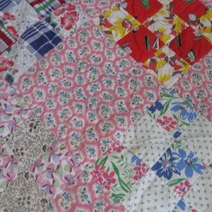 May include: A patchwork quilt featuring a variety of fabric squares with diverse patterns, including pink floral prints, red and yellow floral blocks, blue and white plaid, and white fabric with blue and pink floral designs, finished with a blue border.