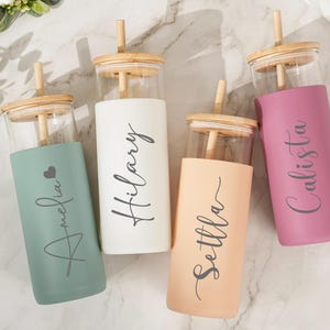 以下が含まれることがあります： 竹製の蓋とストローが付いたガラス製のタンブラー4個。各タンブラーには、Amelia、Hilary、Settla、Calistaと名前がプリントされた色のシリコンスリーブが付いています。色は緑、白、ピーチ、ピンクです。