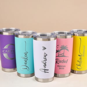 Könnte beinhalten: Sechs isolierte Edelstahlbecher in verschiedenen Farben: Lila, Türkis, Weiß, Rosa und Gelb. Jeder Becher hat einen silbernen Deckel und Boden mit personalisiertem Text in Silber. Die Becher sind für Getränke konzipiert.
