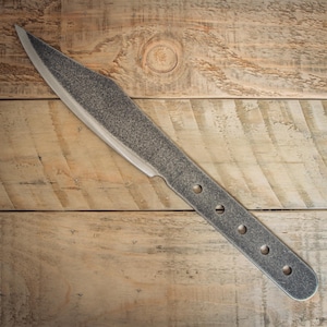 May include: A gray, textured throwing knife with a pointed blade and a handle with four holes. The knife is set against a wooden background.
