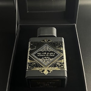 May include: A rectangular black perfume bottle with gold accents and the text "BADEE AL OUD" and "OUD FOR GLORY". The bottle is in a black box with a clear lid. The design features geometric patterns and Arabic script.