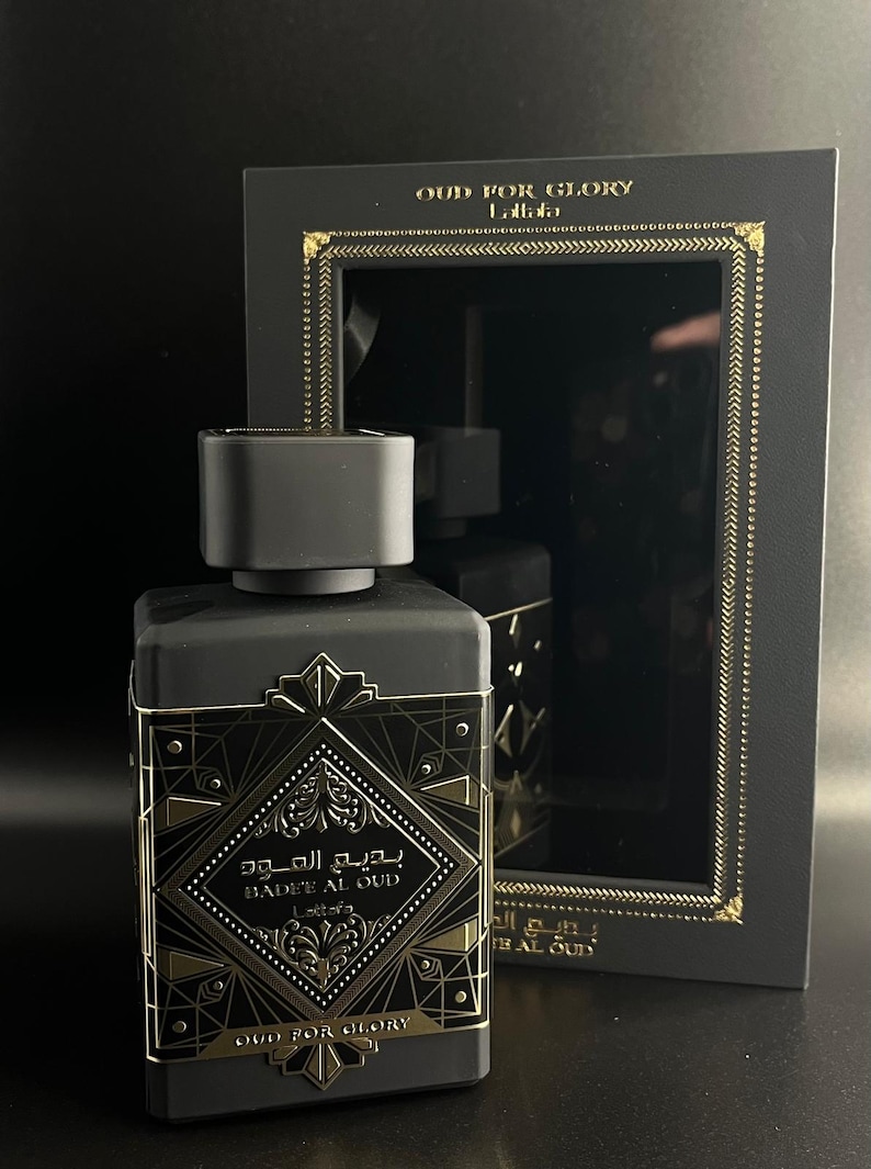 May include: A black perfume bottle with gold accents and the text "BADEE AL OUD" and "OUD FOR GLORY". The bottle is rectangular with a black cap and is displayed in a black box with gold trim.