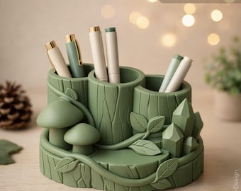 May include: A sage green desk organizer with three pen holders, mushroom and crystal accents, and leaf details. The organizer has the text "STL File Digital Download" and "Commercial License Included". Pens are visible in the holders.
