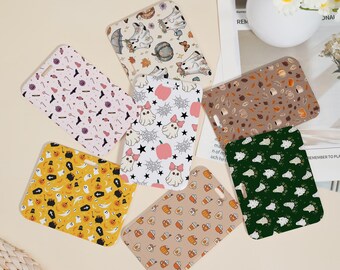 May include: A collection of phone cases with various Halloween-themed patterns. Designs include ghosts, pumpkins, bats, and spiderwebs in colors like orange, pink, and brown. The cases are arranged in a circular pattern.