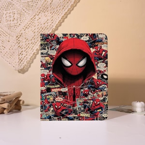 May include: A rectangular Spider-Man themed notebook featuring a red hooded Spider-Man graphic. The background is a collage of comic book panels with the words "Spider-Man" and "Marvel". The notebook is on a white surface.
