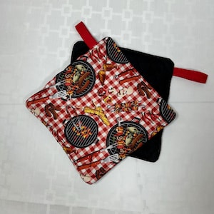 May include: A pair of red and black pot holders with a red and white checkered pattern and a grill theme. The pot holders have a red loop handle.