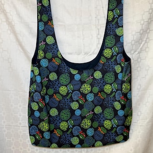 May include: A black tote bag with a repeating pattern of pizza slices and the text "TMNT" in blue, green, and orange. The bag has a dark blue interior and long straps.