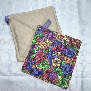 May include: Two square pot holders. One features a vibrant, multi-colored floral print with roses in shades of purple, blue, green, orange, and red. The other is a solid beige quilted fabric with a diamond pattern and a small purple fabric loop.