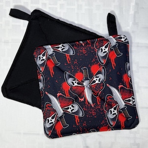 May include: Two square pot holders. One is solid black, the other features a repeating pattern of a butterfly with a Scream mask design and a knife on a black background with red splatter.